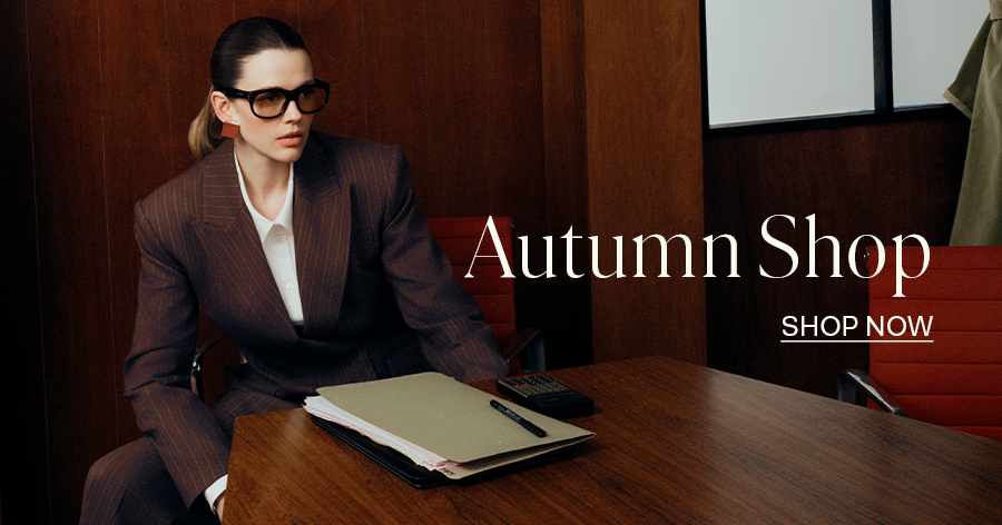Woman in brown pinstripe blazer and black glasses seated at wooden desk with folder, Autumn Shop fashion advertisement