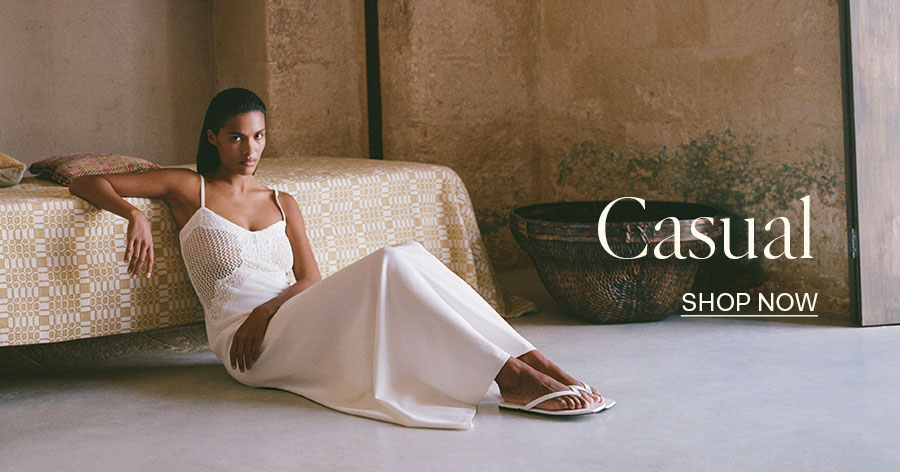 Woman in white crochet top, maxi skirt, and sandals seated on floor beside a patterned sofa, "Casual Shop Now" text overlay