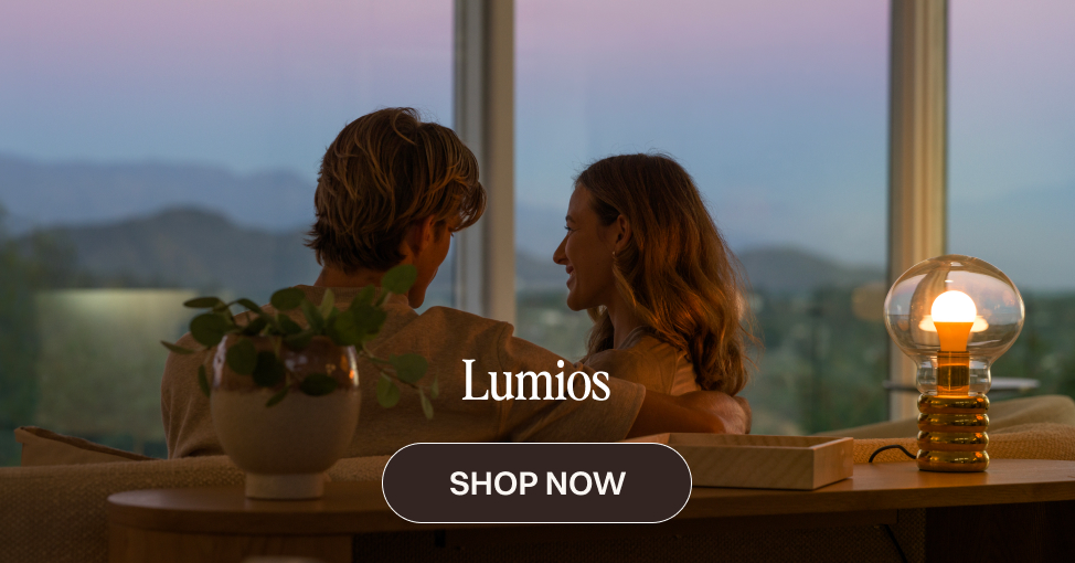 Two people sitting together near a Lumios table lamp at dusk, with a mountain view through large windows.