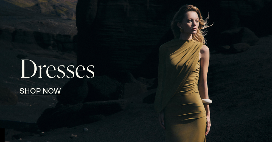 Woman in elegant gold one-shoulder draped dress posing outdoors, with "Dresses - Shop Now" text overlay