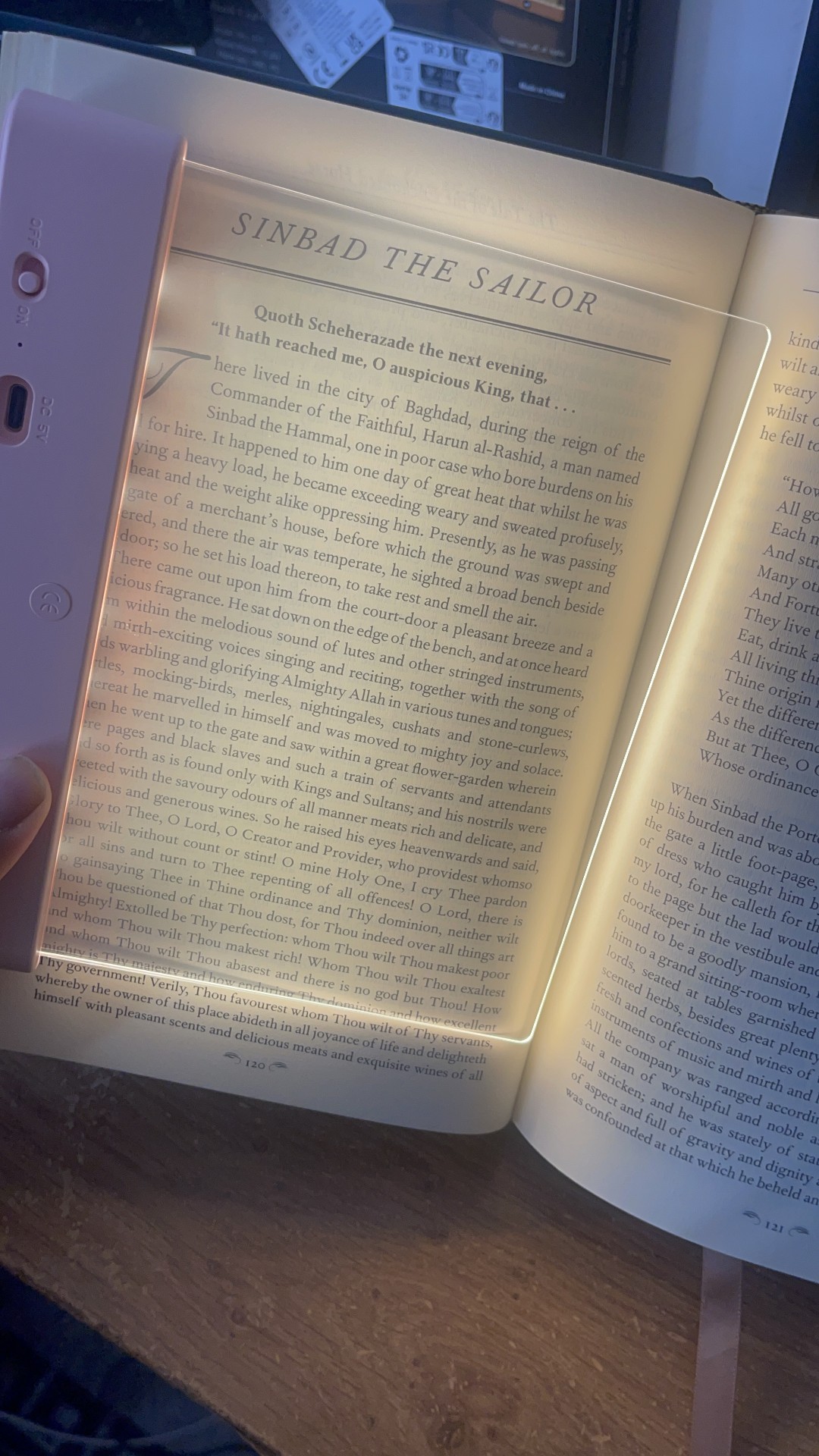 Open book showing "Sinbad the Sailor" chapter with an LED reading light panel illuminating the pages 120-121.