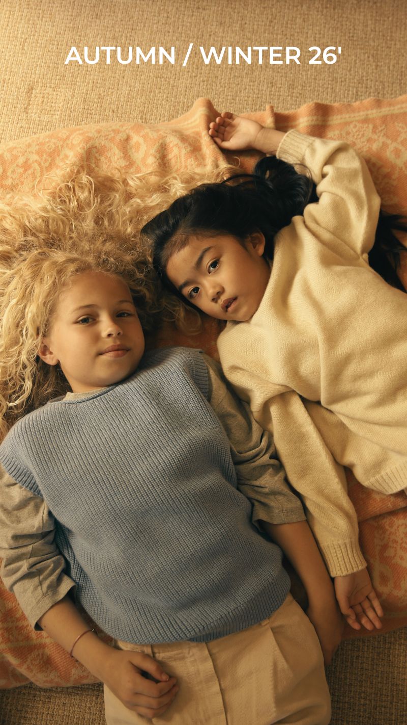Two children lying on a blanket wearing knit sweaters, Autumn/Winter 26' kids fashion collection campaign