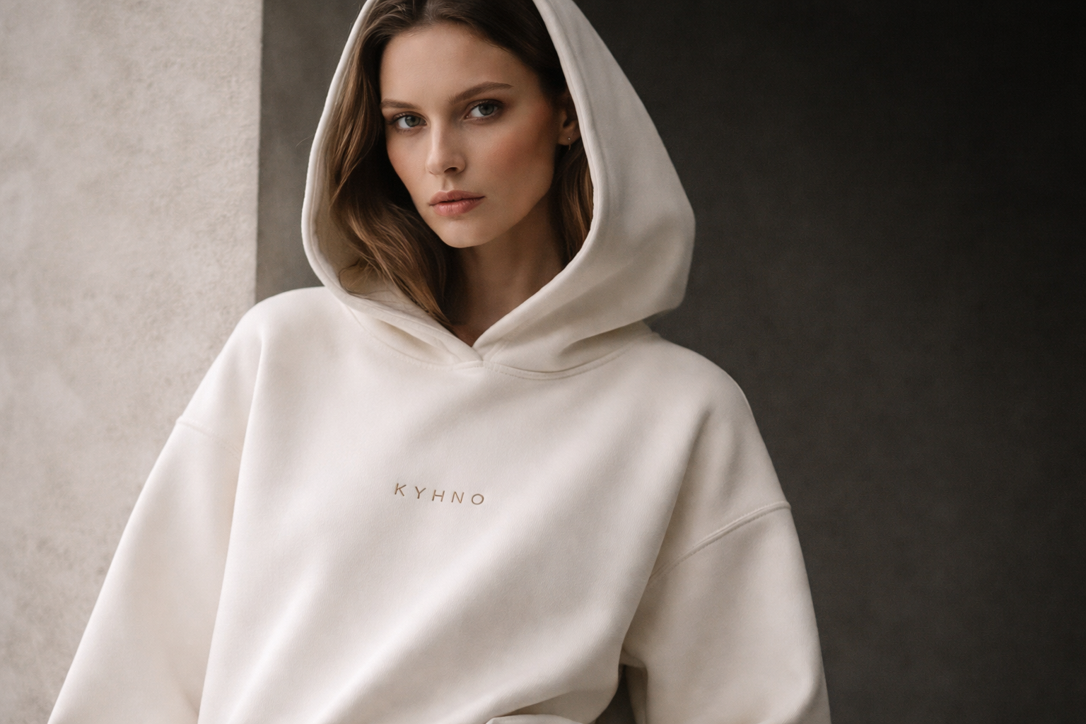 A person wearing a cream-colored hoodie with "KYHNO" written on it, standing against a neutral background. The person's face is blurred.