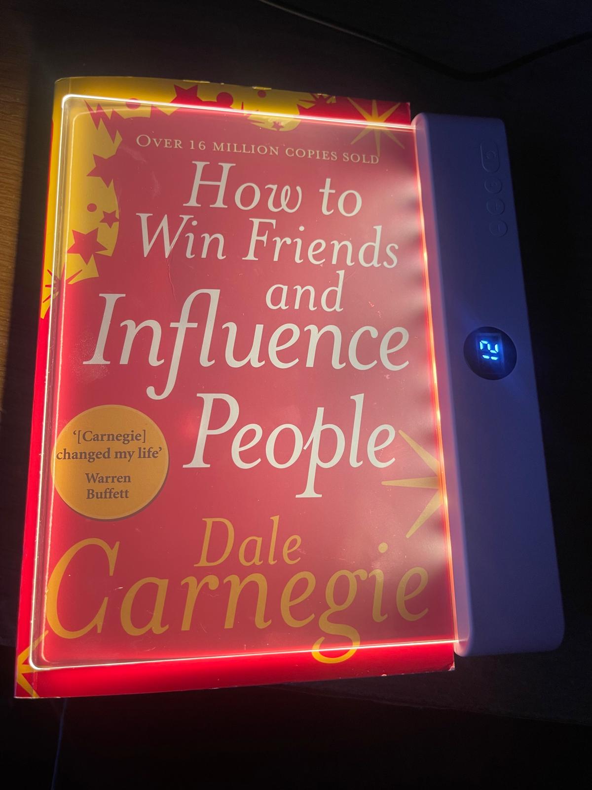 "How to Win Friends and Influence People" by Dale Carnegie book with red cover on a light pad