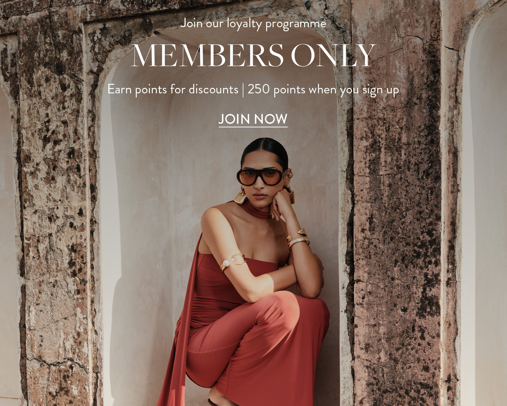 ```html
<img src="image.jpg" alt="Person in red outfit sitting near an old stone wall with promotional text for a loyalty programme." />
```