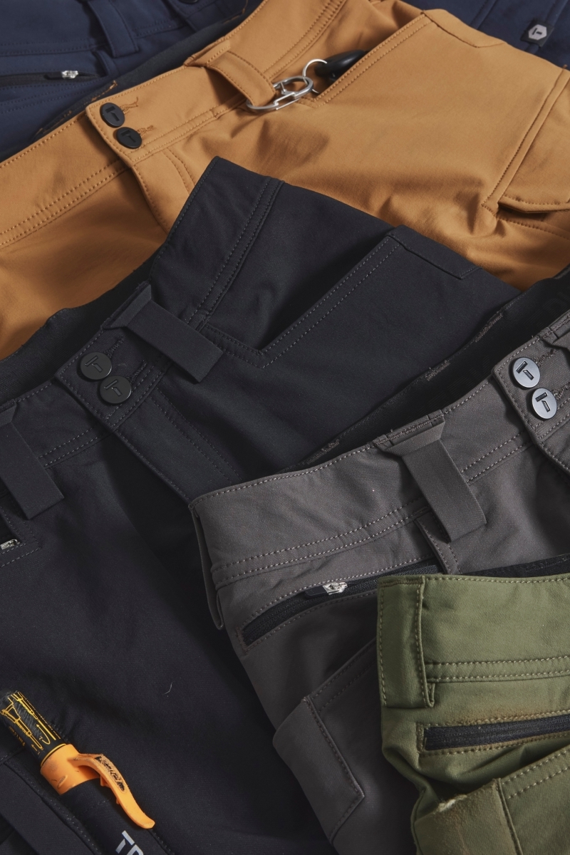 A close-up shot of various pairs of tactical trousers in different colors, including brown, black, gray, and green, featuring multiple pockets and button closures.