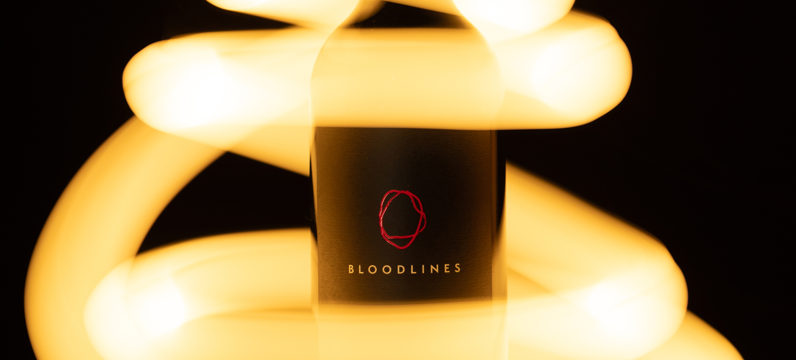 "Bloodlines" branded black wine bottle label with red loop logo, surrounded by glowing golden light trails on dark background