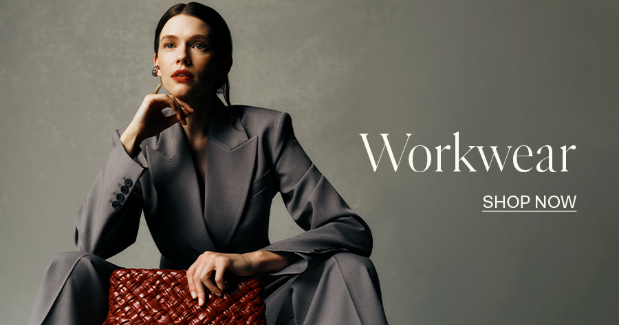 Woman in gray tailored suit holding a woven brown leather clutch, workwear fashion advertisement with "Shop Now" text.