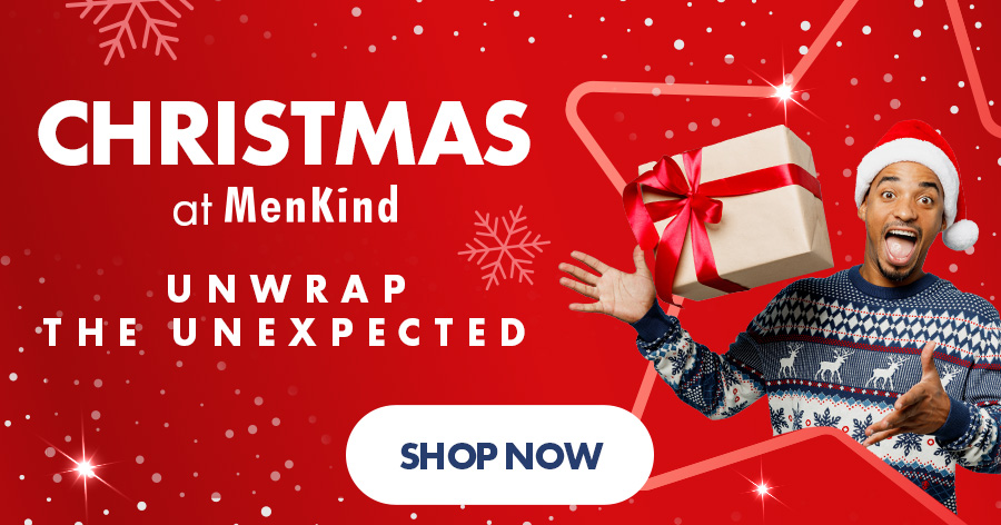 Man in Santa hat and Christmas sweater holding gift box, MenKind holiday ad reading "Unwrap the Unexpected"