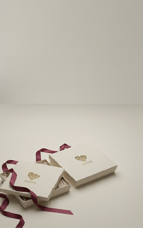 Two cream-colored Avaha gift boxes with gold logo and burgundy satin ribbons on a neutral background