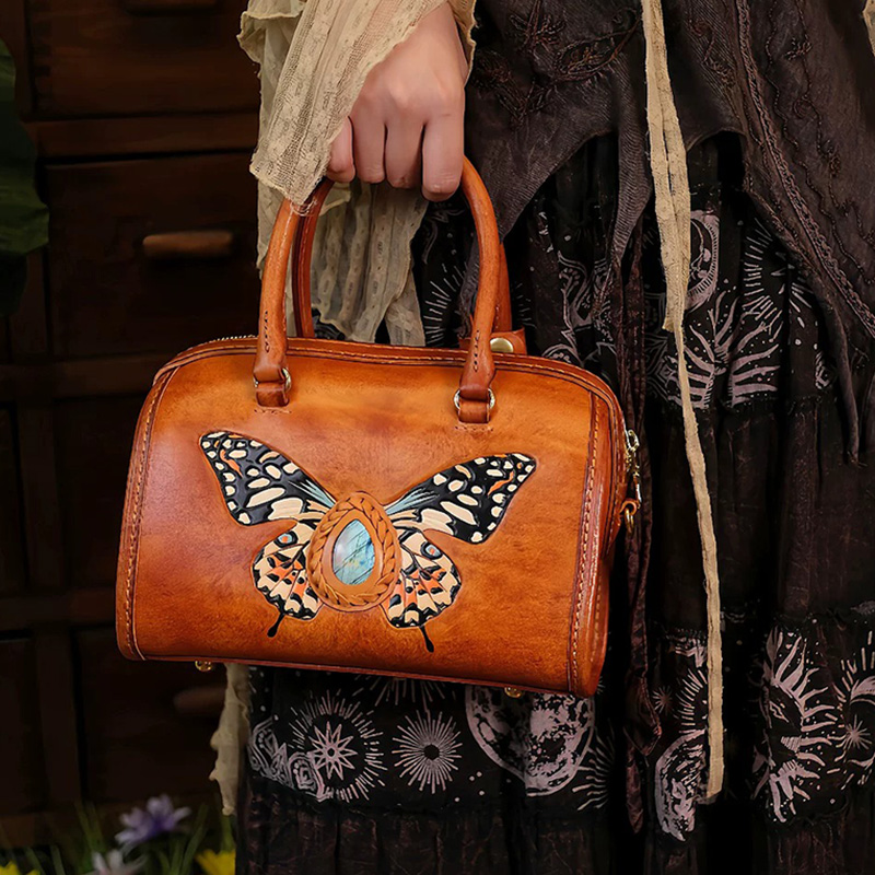 Brown leather handbag with butterfly embossed design and gemstone accent, held by a woman in a patterned skirt