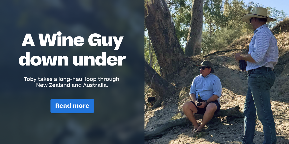 ```html
<img src="image.jpg" alt="Two men in a natural setting, one sitting on a log with a bottle, and the other standing holding a drink. Trees and sunlight in the background. Text reads: 'A Wine Guy down under. Toby takes a long-haul loop through New Zealand and Australia. Read more.'">
```