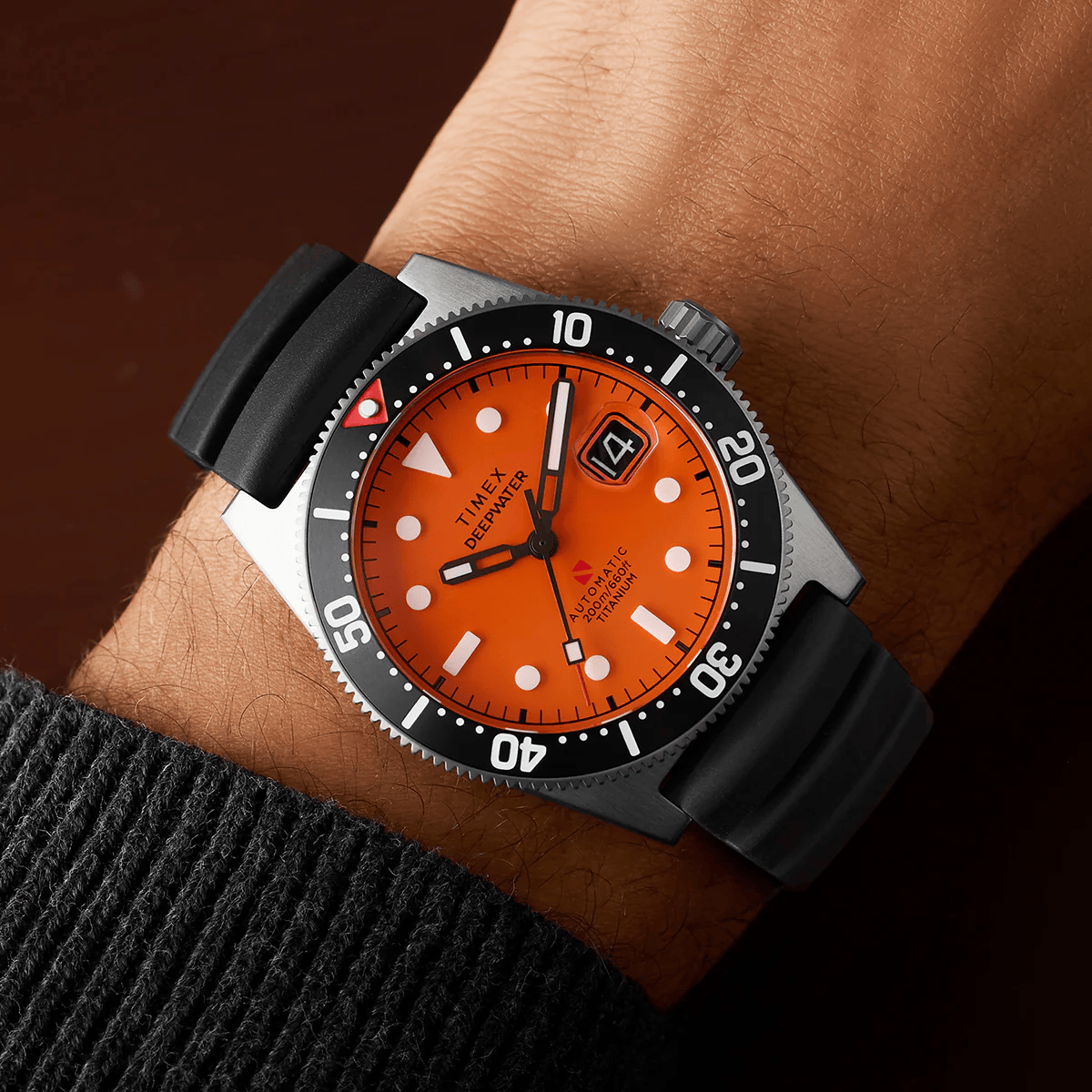 ```html
<img src="watch.jpg" alt="Orange Timex watch with black bezel and rubber strap on wrist, showing time and date." />
```