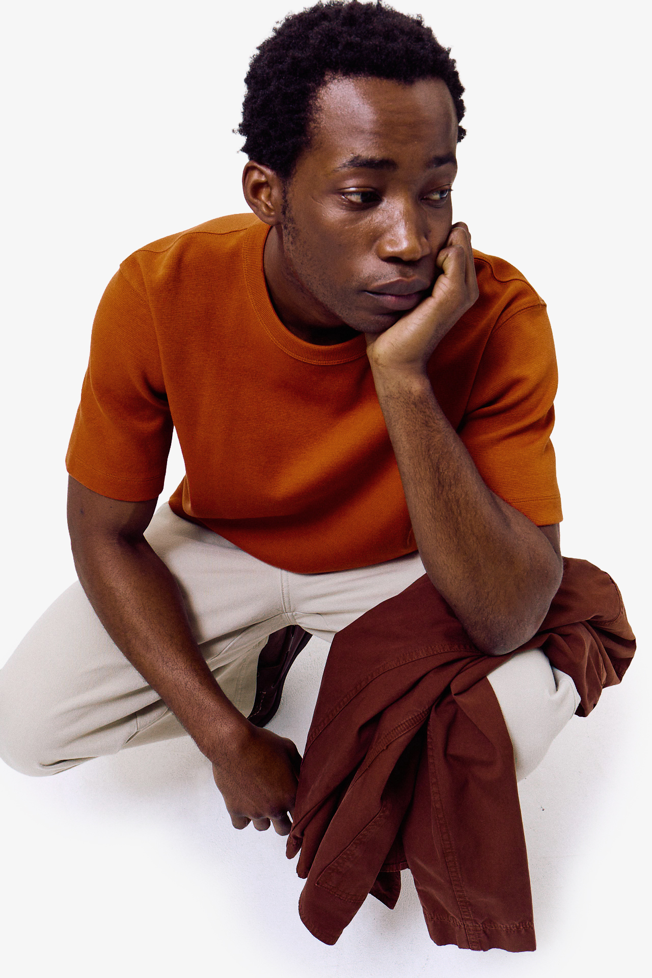 ```html
<img src="image.jpg" alt="Person wearing an orange shirt and beige pants, holding a brown jacket, face blurred." />
```