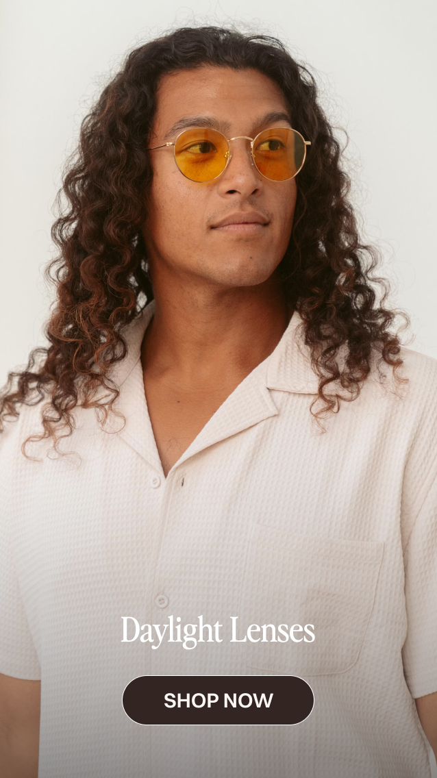 Man with long curly hair wearing round yellow-tinted sunglasses and a white textured shirt, promoting Daylight Lenses