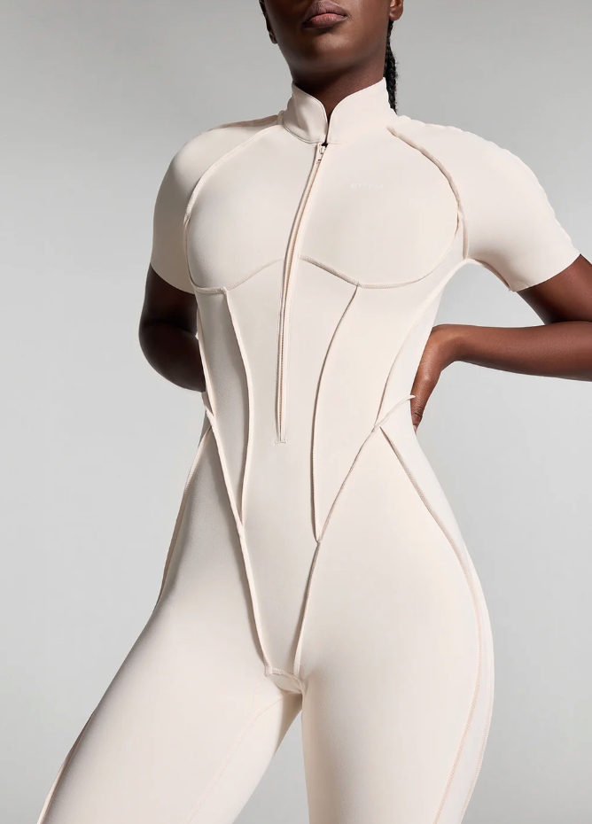 ```html
<img src="image.jpg" alt="Person wearing a beige fitted jumpsuit with short sleeves and a front zipper.">
```