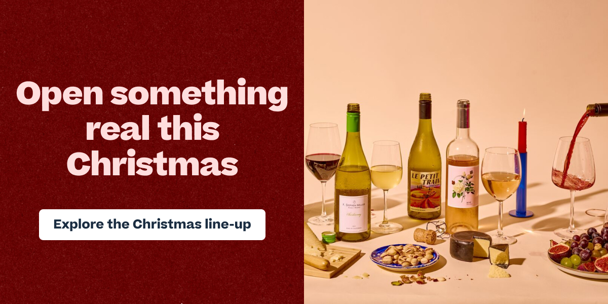 Christmas wine advertisement featuring three wine bottles, filled glasses, cheese, grapes, and nuts on a table with a candle