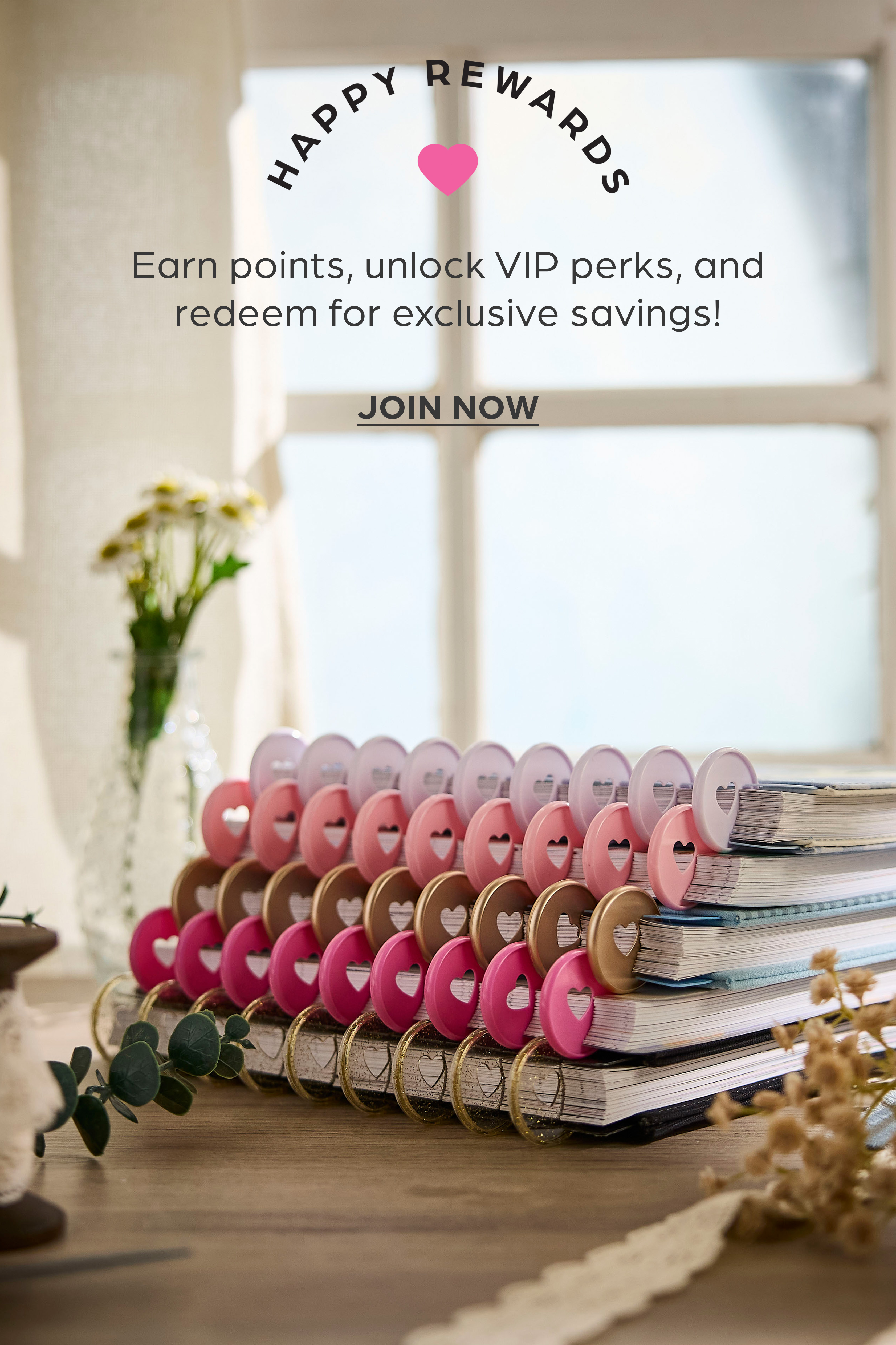 ```html
<img src="image.jpg" alt="Stack of notebooks with colorful covers and heart-shaped designs, promotional text for Happy Rewards program offering points, VIP perks, and savings. Decorative vase with flowers in the background." />
```