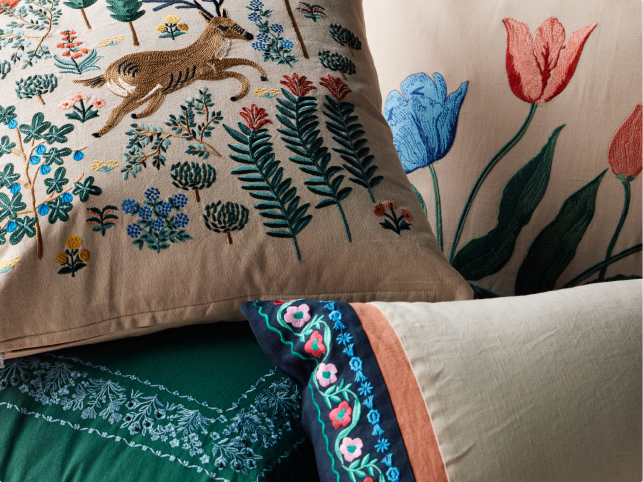 ```html
<img src="image.jpg" alt="Decorative pillows with embroidered designs of a deer and floral patterns in various colors." />
```