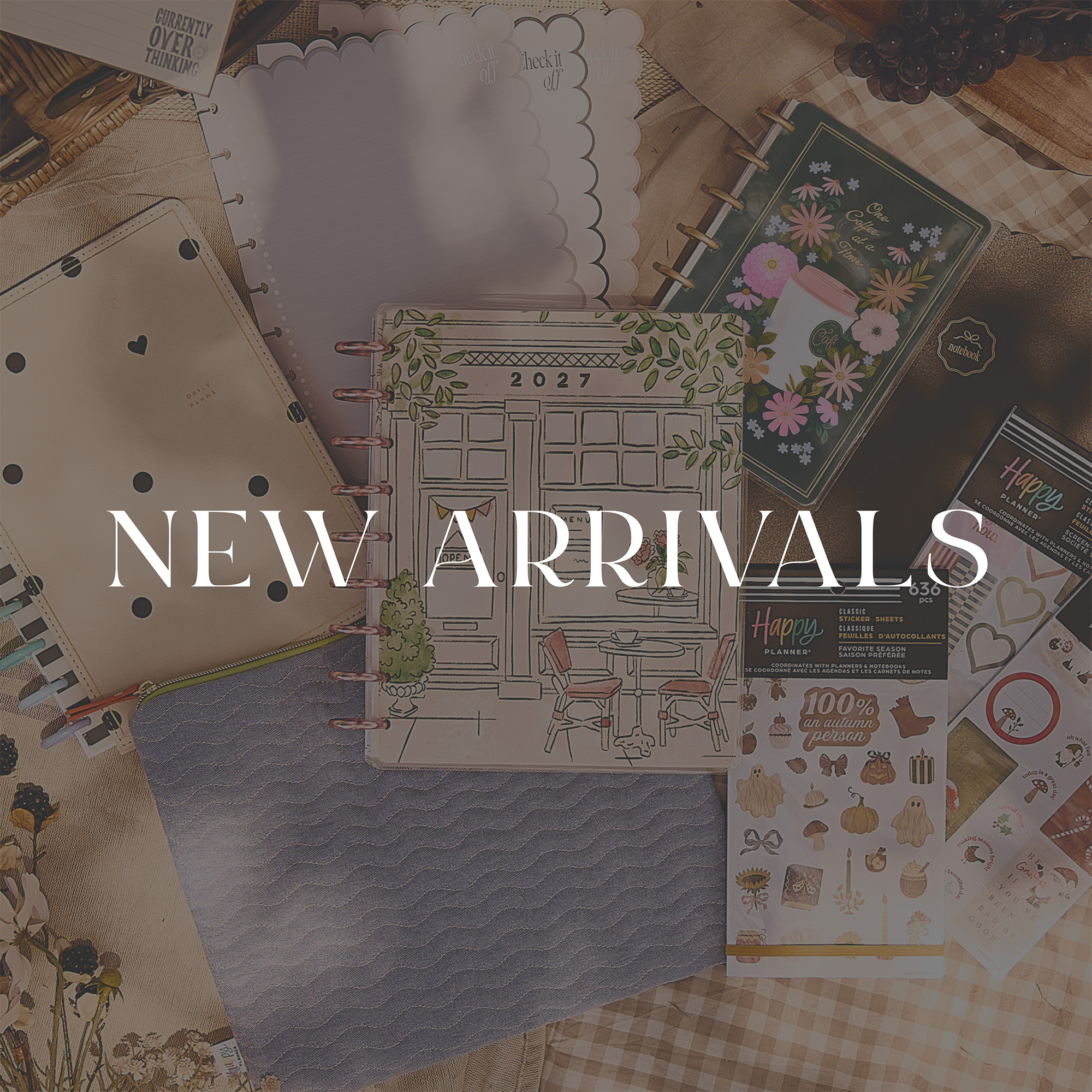 "New Arrivals" text overlay on a flat lay of Happy Planner products, including a 2027 planner, sticker sheets, and notebooks.