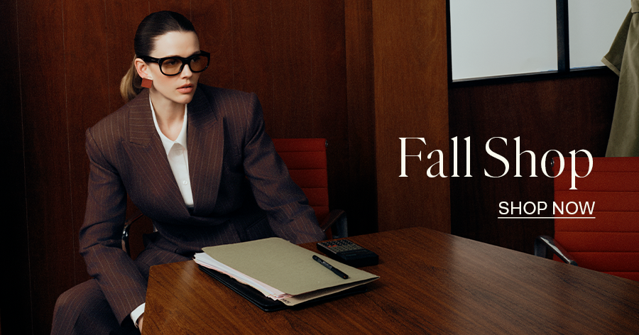 Woman in brown pinstripe suit and oversized glasses seated at wooden desk in office, Fall Shop advertisement