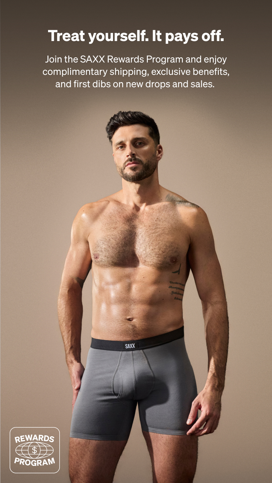 A shirtless man wearing gray SAXX underwear stands against a beige background. Text promotes the SAXX Rewards Program.
