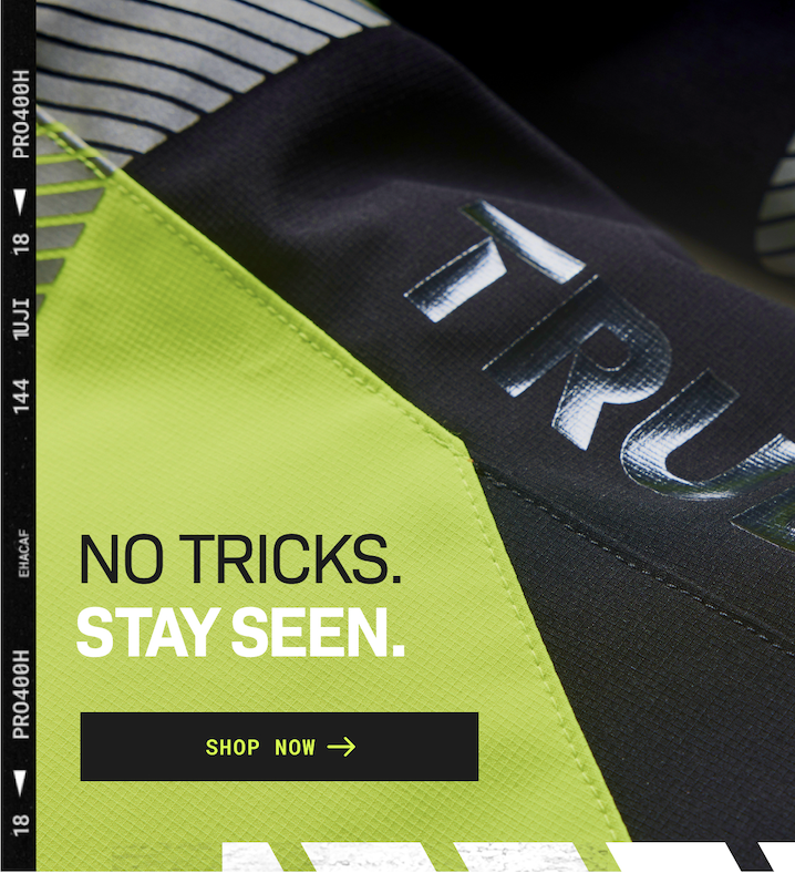 Close-up of a high-visibility fabric with text "NO TRICKS. STAY SEEN." and a "SHOP NOW" button, emphasizing visibility and safety.